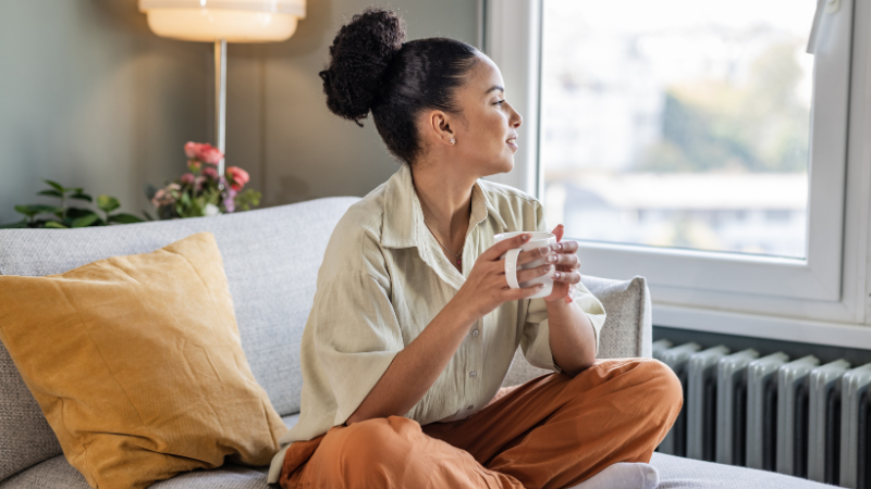 Lady sitting on sofa drinking a hot drink looking out of the window