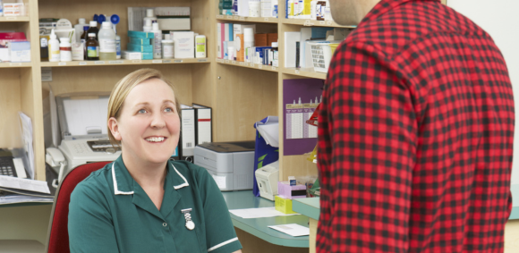 A female registered veterinary nurse sitting behind a reception desk interacting with a male client