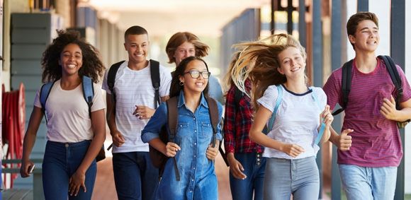 A group of young adults with backpacks and casual clothing walking out of a school hallway